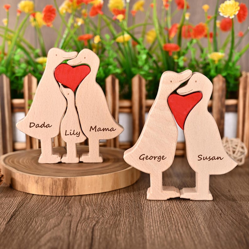 May include: Wooden family duck figurines with a red heart in the centre. One set has the names "Dada", "Lily", and "Mama" engraved. The other set has "George" and "Susan" engraved. The ducks are light brown.