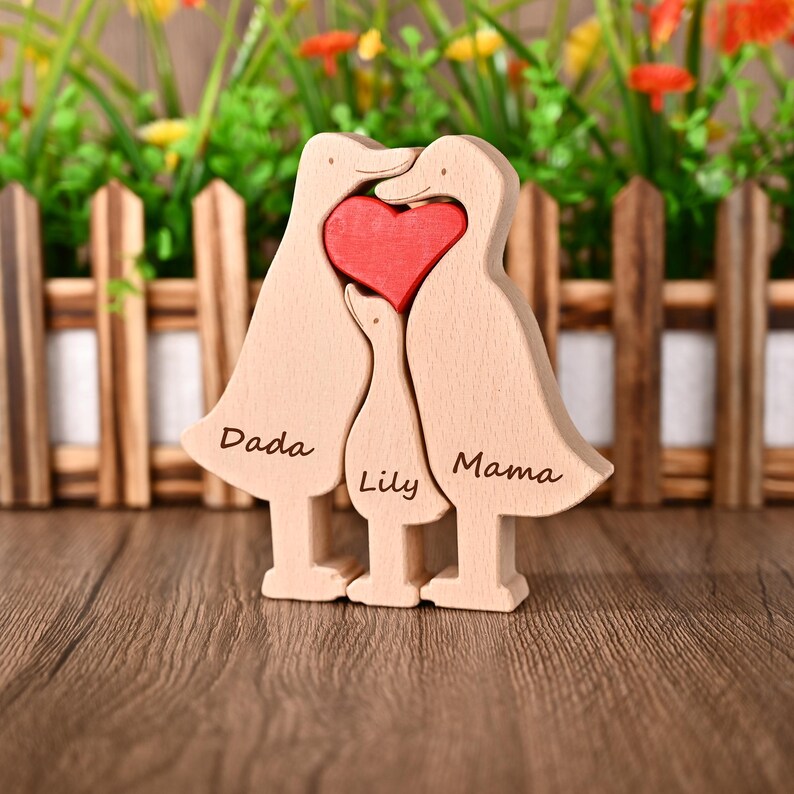 May include: Wooden family duck ornament featuring a red heart. The ducks are light brown, with the words "Dada", "Lily", and "Mama" engraved. The ornament is displayed on a wooden surface.