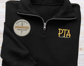 May include: Black quarter-zip sweatshirt with gold embroidered "PTA" and "andrews" text. Features a round patch that says "Personalize it! Embroidered Comfort Colors". The sweatshirt has a ribbed cuff and a silver zipper.