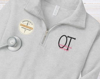 May include: A light gray quarter-zip sweatshirt with the embroidered letters "OT" and the words "Occupational Therapist" in pink. A stethoscope and a circular patch that says "Personalize it! Embroidered Comfort Colors" are also visible.