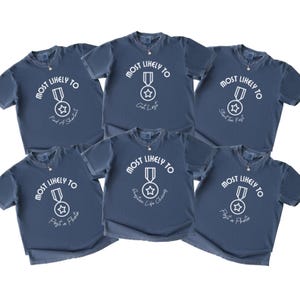 May include: Six navy blue t-shirts with the text "MOST LIKELY TO" above a medal graphic. Each shirt has a different phrase below the graphic: "Find a Shortcut", "Get Lost", "Start Too Fast", "Question Life Choices", and "Post a Photo".