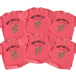 May include: Six coral-colored t-shirts with black text and green footprint graphics. Each shirt has a different phrase: "Need a Bathroom Break," "Stop for Photos," "Kiss a Stranger," "Prom Accident," "Take a Photo," and "Find a Shortcut."