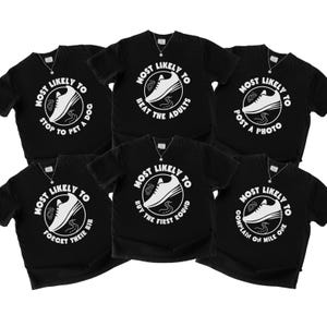 May include: Six black t-shirts with white graphic designs. Each shirt features a running shoe illustration inside a circle with the words "MOST LIKELY TO" above and a different phrase below, such as "STOP TO PET A DOC".