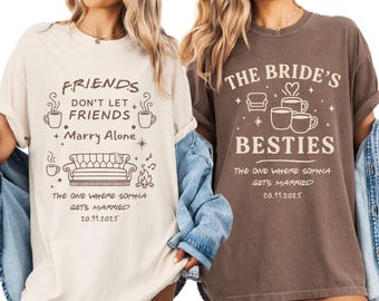 Puede incluir: Dos camisetas, una crema y otra marrón, con diseños gráficos a juego. La camiseta crema dice "FRIENDS don't let friends marry alone" con un sofá y tazas de café. La camiseta marrón dice "The Bride's Besties". Ambas camisetas tienen la fecha 20.11.2025.