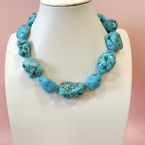 Puede incluir: Un collar compuesto por grandes piedras de turquesa pulidas e irregulares que presentan vetas de matriz de color marr&oacute;n oscuro. Las piedras est&aacute;n ensartadas en una sola hebra, mostrando un vibrante color azul cielo con variaciones naturales de forma y textura en toda la pieza.