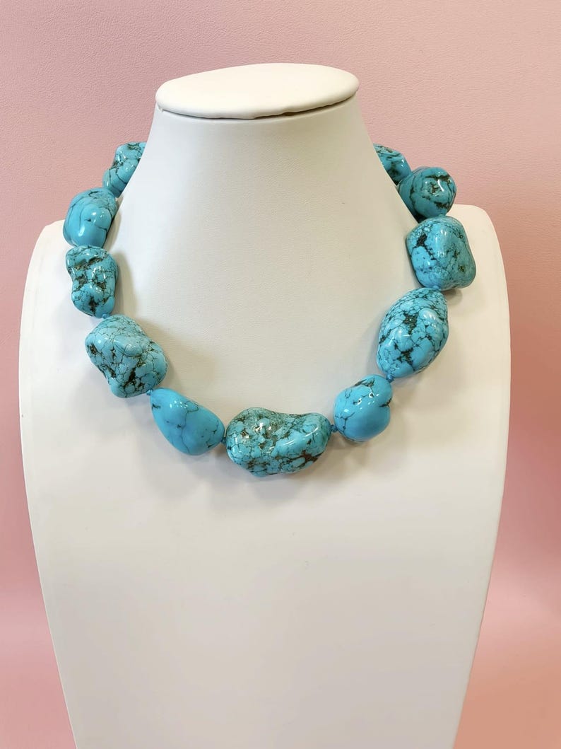 Puede incluir: Un collar compuesto por grandes piedras de turquesa pulidas e irregulares que presentan vetas de matriz de color marr&oacute;n oscuro. Las piedras est&aacute;n ensartadas en una sola hebra, mostrando un vibrante color azul cielo con variaciones naturales de forma y textura en toda la pieza.