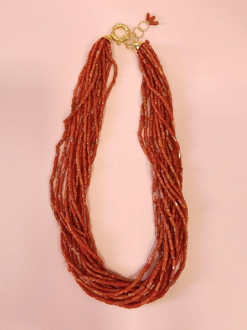 Pode incluir: Um colar de v&aacute;rias voltas composto por pequenas contas vermelho-alaranjadas. O colar &eacute; preso com um fecho dourado e tem uma apar&ecirc;ncia delicada e elegante. As contas s&atilde;o enfiadas juntas, criando um efeito de cascata.