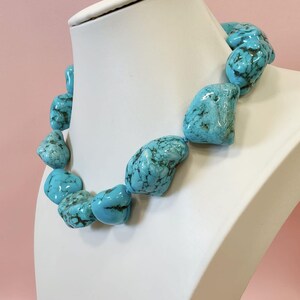 Puede incluir: Un collar compuesto por piedras de turquesa grandes, irregulares y pulidas que presentan vetas de matriz de color marr&oacute;n oscuro. Las piedras est&aacute;n ensartadas en una sola hebra, mostrando un color azul cielo vibrante con variaciones naturales en forma y tama&ntilde;o.