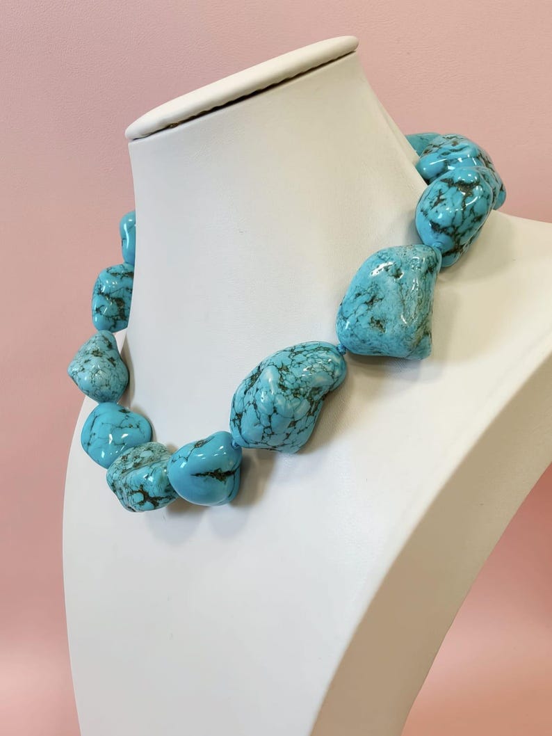 Puede incluir: Un collar compuesto por piedras de turquesa grandes, irregulares y pulidas que presentan vetas de matriz de color marr&oacute;n oscuro. Las piedras est&aacute;n ensartadas en una sola hebra, mostrando un color azul cielo vibrante con variaciones naturales en forma y tama&ntilde;o.
