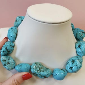 Puede incluir: Un collar compuesto por grandes piedras de turquesa pulidas e irregulares que presentan vetas de matriz de color marr&oacute;n oscuro. Las vibrantes piedras de color azul verdoso est&aacute;n ensartadas en una sola hebra, creando una pieza de joyer&iacute;a llamativa.