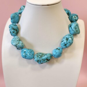Puede incluir: Un collar compuesto por piedras de turquesa grandes, irregulares y pulidas. Cada piedra presenta un color azul cielo vibrante con vetas de matriz de color marr&oacute;n oscuro. Las piedras est&aacute;n ensartadas para formar un collar continuo y grueso.
