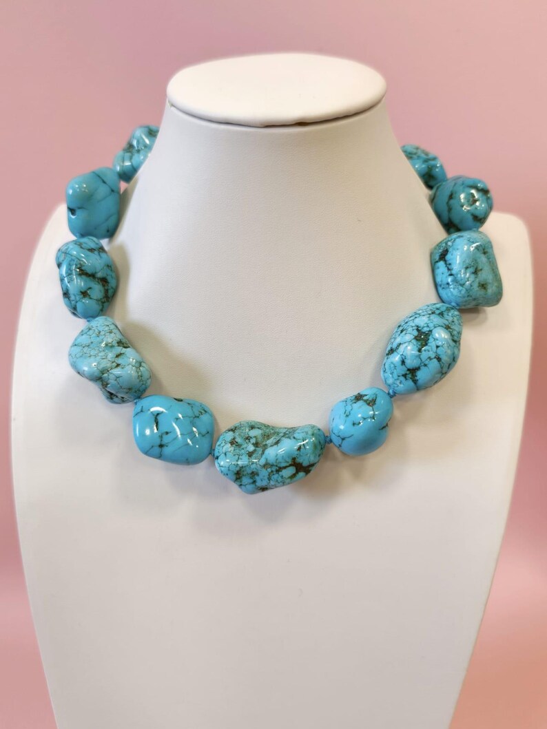 Puede incluir: Un collar compuesto por piedras de turquesa grandes, irregulares y pulidas. Cada piedra presenta un color azul cielo vibrante con vetas de matriz de color marr&oacute;n oscuro. Las piedras est&aacute;n ensartadas para formar un collar continuo y grueso.