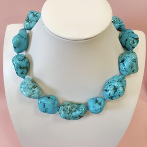 Puede incluir: Un collar compuesto por piedras de turquesa grandes, irregulares y pulidas que presentan vetas de matriz de color marr&oacute;n oscuro y negro. Las piedras est&aacute;n ensartadas en una sola hebra, mostrando un vibrante color azul cielo con variaciones naturales en forma y tama&ntilde;o.