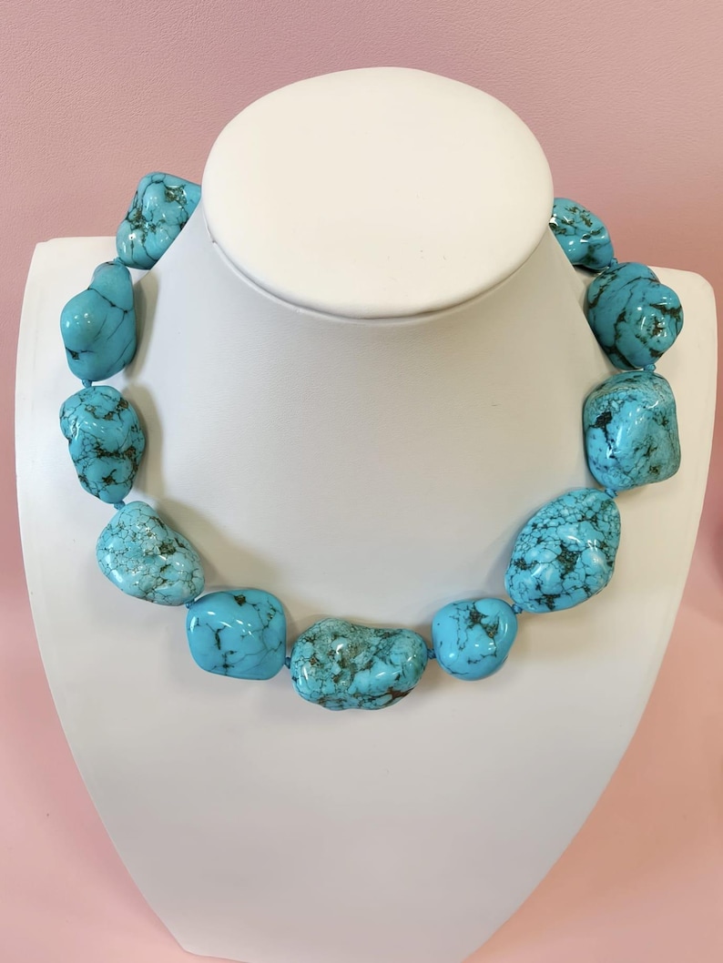 Puede incluir: Un collar compuesto por piedras de turquesa grandes, irregulares y pulidas que presentan vetas de matriz de color marr&oacute;n oscuro y negro. Las piedras est&aacute;n ensartadas en una sola hebra, mostrando un vibrante color azul cielo con variaciones naturales en forma y tama&ntilde;o.