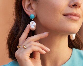 May include: Dangle earrings featuring a square-cut turquoise stone set in gold-tone metal, with a large, irregular white baroque pearl suspended beneath. Two simple gold-tone bands are worn on the fingers, complementing the jewelry set.