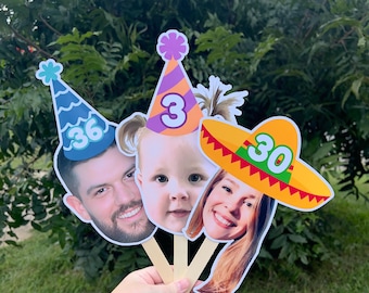 May include: Three custom photo face cutouts on wooden sticks. The left cutout shows a man wearing a blue party hat with the number 36. The center cutout shows a child wearing a purple and orange party hat with the number 3. The right cutout shows a person wearing a yellow sombrero with the number 30.