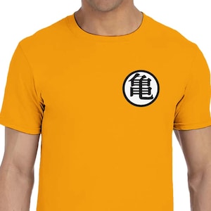 Puede incluir: Camiseta de color amarillo mostaza con un gráfico circular en blanco y negro en el pecho. El gráfico es un símbolo japonés estilizado. La camiseta tiene mangas cortas y cuello redondo.