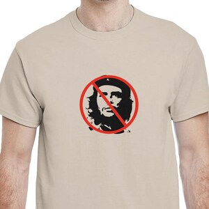 Puede incluir: Una camiseta color beige con un gráfico negro y rojo. El gráfico es una silueta de la cara de una persona dentro de un círculo rojo con una línea roja. La camiseta está hecha de un material suave.