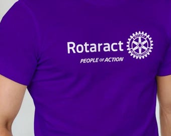 May include: A purple t-shirt featuring the word "Rotaract" in white, the text "PEOPLE OF ACTION", and a white logo. The logo is a gear design with the words "ROTARY INTERNATIONAL".
