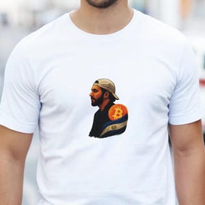 Puede incluir: Camiseta blanca con un gráfico de un hombre con gorra de béisbol, un símbolo de Bitcoin y un diseño de bandera. El gráfico está en el área del hombro izquierdo de la camiseta.