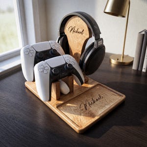 May include: A wooden gaming organiser stand featuring a vertical headphone hanger and two slots for white game controllers. The wood surface is engraved with the name Michael on both the headphone stand and the base tray, which holds two controllers.