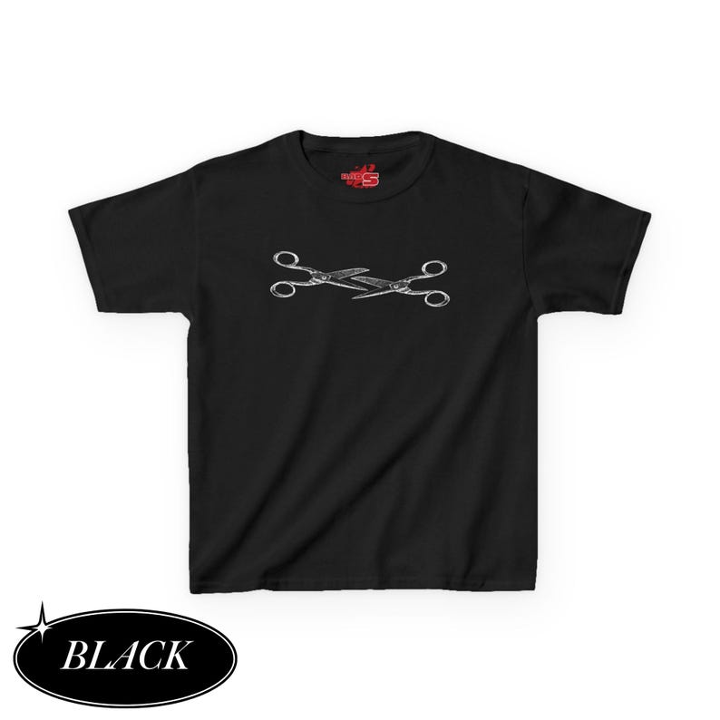 May include: Black t-shirt featuring a white graphic of two crossed scissors. The shirt has short sleeves and a crew neck. The word "BLACK" is in a black oval at the bottom left.