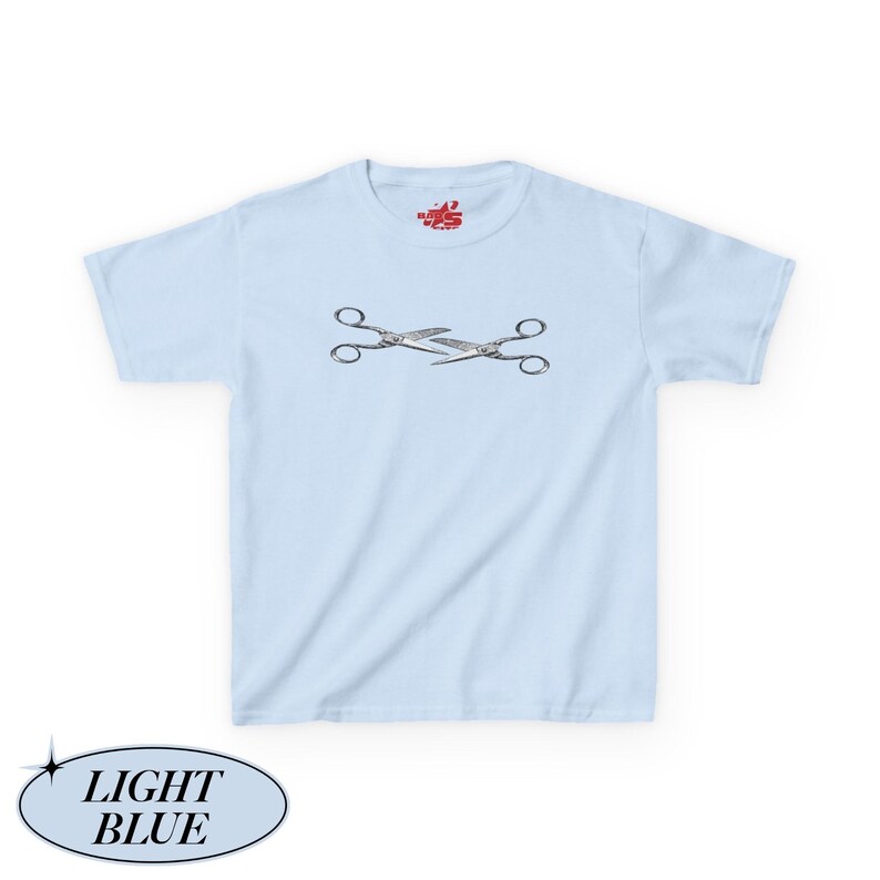 May include: Pale blue t-shirt featuring a mirrored pair of scissors in silver and black. The shirt has a crew neck and short sleeves. The text "LIGHT BLUE" is in a light blue oval at the bottom left.