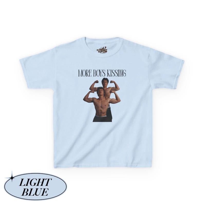 May include: Light blue t-shirt with the text "MORE BOYS KISSING" above a graphic of two shirtless men. The shirt also has a small logo near the neckline and the words "LIGHT BLUE" in a light blue oval.
