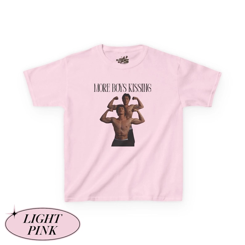 May include: Light pink t-shirt with the text "MORE BOYS KISSING" above a graphic of two shirtless men flexing. The shirt also has the words "LIGHT PINK" in a decorative oval at the bottom.