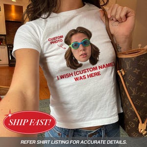 Op de afbeelding: Een wit t-shirt met korte mouwen en een aangepaste foto van een persoon met een groen-blauwe zwembril. De tekst CUSTOM PHOTO met een pijl en de zin I WISH (CUSTOM NAME) WAS HERE zijn in het rood op de voorkant van het shirt gedrukt.