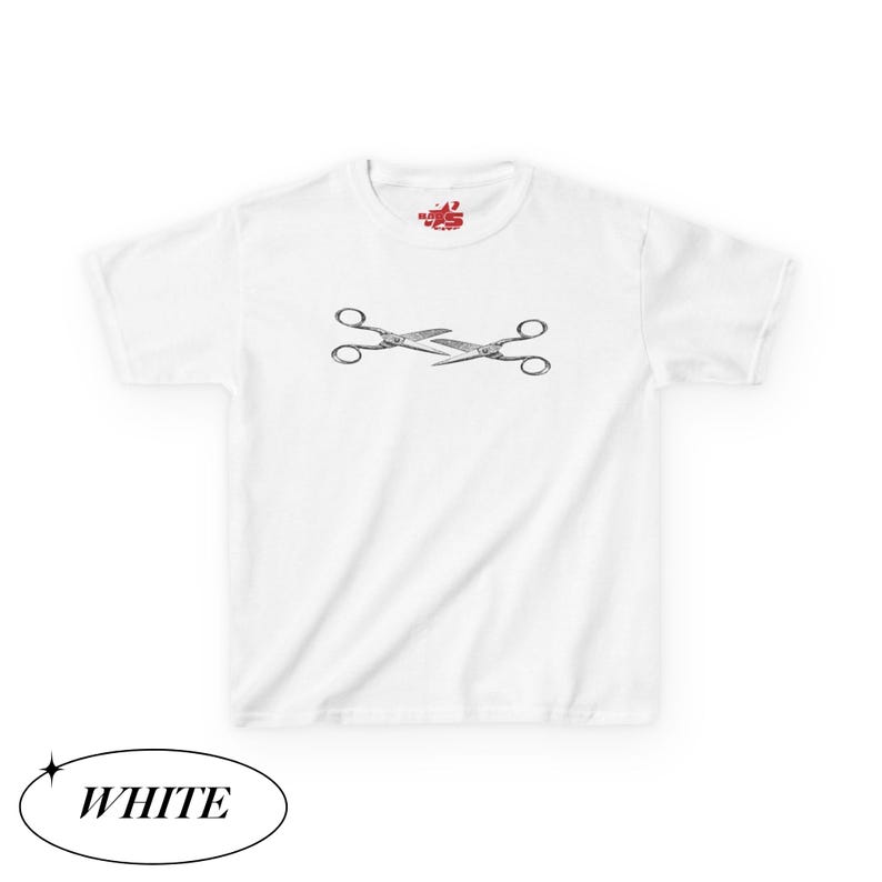 May include: White t-shirt featuring a black and white illustration of crossed scissors. The shirt has a crew neck and short sleeves. The word "WHITE" is in a white oval at the bottom of the image.