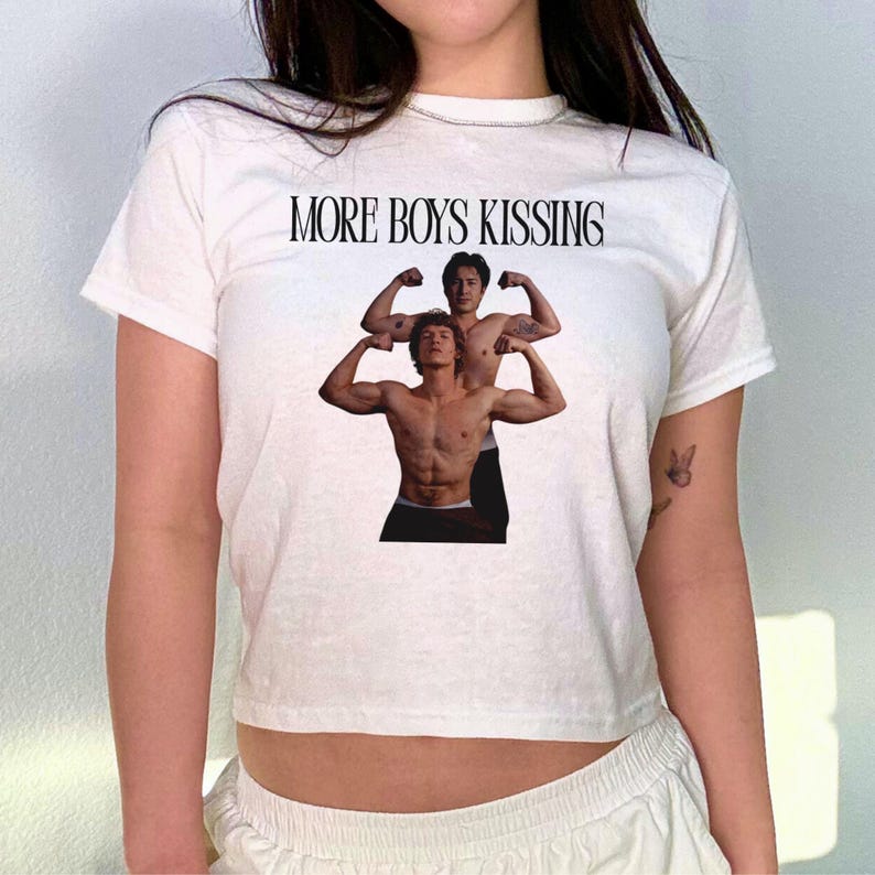 May include: White crop top with the text "MORE BOYS KISSING" in black. The shirt features a graphic of two muscular men flexing their biceps. The top is short-sleeved and has a crew neck.