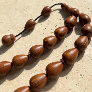 Puede incluir: Primer plano de un collar de cuentas de oraci&oacute;n de madera marr&oacute;n. Las cuentas tienen forma de l&aacute;grima y est&aacute;n ensartadas en un cord&oacute;n negro. Las cuentas tienen un acabado liso y pulido y var&iacute;an ligeramente de color.