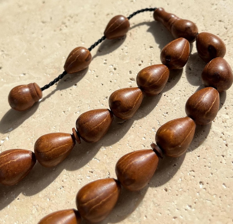 Puede incluir: Primer plano de un collar de cuentas de oraci&oacute;n de madera marr&oacute;n. Las cuentas tienen forma de l&aacute;grima y est&aacute;n ensartadas en un cord&oacute;n negro. Las cuentas tienen un acabado liso y pulido y var&iacute;an ligeramente de color.