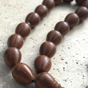 Puede incluir: Un rosario de madera marr&oacute;n. Las cuentas ovaladas tienen una superficie texturizada y est&aacute;n ensartadas con un cord&oacute;n negro. Las cuentas son de color marr&oacute;n c&aacute;lido.