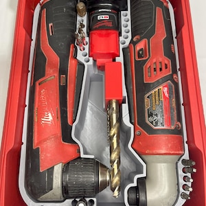 May include: A red and black Milwaukee M12 cordless drill and impact driver set in a red case. The set includes various drill bits and accessories, and a battery pack. The tools are arranged in a gray insert within the case.