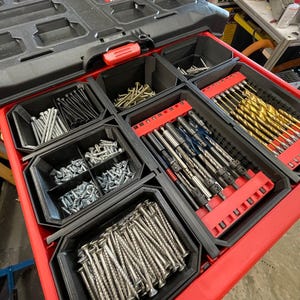 May include: A red and black Milwaukee tool box with an open drawer filled with various screws, drill bits, and other hardware. The drawer is divided into compartments for organization. The Milwaukee logo is visible on the top of the toolbox.