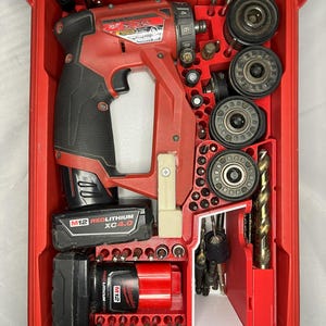 Op de afbeelding: Een rode koffer met een rode en zwarte Milwaukee M12 RedLithium XC 4.0 accuschroefboormachine, batterijen en diverse boren en opzetstukken. Alles is georganiseerd in een rode koffer.