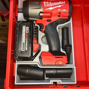 Könnte beinhalten: Ein roter und schwarzer Milwaukee FUEL Schlagschrauber mit Akku und Steckschlüsseln in einer roten Werkzeugkiste. Der Akku ist mit "M18 REDLITHIUM HIGH OUTPUT XC6.0" beschriftet. Das Milwaukee-Logo ist deutlich sichtbar.