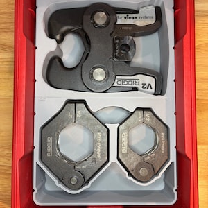 May include: A red toolbox containing a black Ridgid ProPress tool and two gray V2 ProPress jaws. The tool is labeled "for viega systems" and "RIDGID V2". The jaws are labeled "2" and "1-1/2".