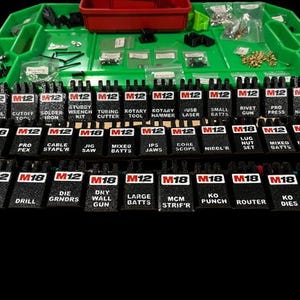 Puede incluir: Un organizador de herramientas verde y rojo lleno de varias herramientas y accesorios. Las etiquetas negras de las herramientas con texto blanco están dispuestas en filas, incluyendo etiquetas "M12" y "M18". Las etiquetas indican diferentes tipos de herramientas.