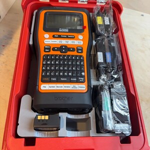 May include: A red, hard-shell case containing a black and orange Brother P-touch EDGE label maker. The label maker has a QWERTY keyboard and a small screen. Several label cartridges and a battery pack are also included.