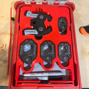 May include: A red Ridgid ProPress tool kit with various black and silver press tool attachments. The kit includes a large press tool, several smaller attachments, and two Sharpie markers. The case is open, revealing the tools neatly organized.