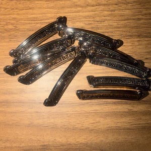 Può includere: Una collezione di fermagli per capelli in metallo argentato con la scritta incisa "CHROME HEARTS" disposti su una superficie di legno. I fermagli hanno un design curvo e una finitura lucida, che riflette la luce.