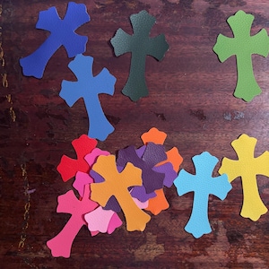 以下が含まれることがあります： 青、緑、ピンク、オレンジ、黄色など、さまざまな色合いのカラフルな革製の十字架のコレクション。 十字架は暗い木製の表面に配置されており、鮮やかな表示になっています。 クラフトや宗教的なテーマに最適です。