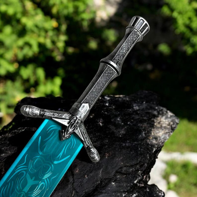 May include: A detailed close-up of a fantasy sword with a teal blade and ornate silver handle. The blade features engraved designs, and the handle has intricate patterns. The sword is resting on a dark, textured surface, with a blurred green background.