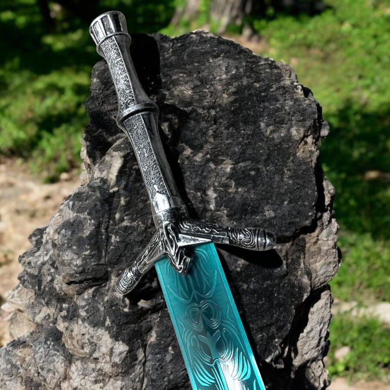 May include: A decorative sword with a silver handle and a blue blade. The handle features intricate designs, and the blade has a patterned surface. The sword is displayed against a dark, textured background, suggesting a fantasy or historical theme.