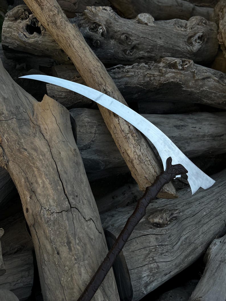 May include: A silver scythe blade with a curved design and a dark brown handle. The handle has a textured, carved appearance. The scythe is set against a backdrop of weathered wooden logs, creating a rustic aesthetic.