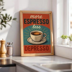 Pode incluir: Uma impressão emoldurada em estilo vintage com as palavras "more espresso less depresso" em uma fonte retrô. A obra de arte apresenta uma xícara de café em um pires, em um fundo vermelho e azul-petróleo, emoldurada em madeira clara.