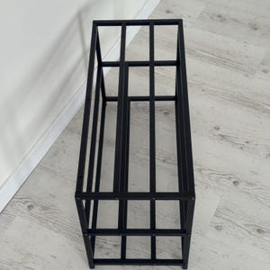 Op de afbeelding: Zwart metalen opbergrek met een rechthoekig frame en verticale en horizontale staven. Het open ontwerp maakt gemakkelijke toegang en weergave van items mogelijk. Geschikt voor diverse opslagbehoeften.